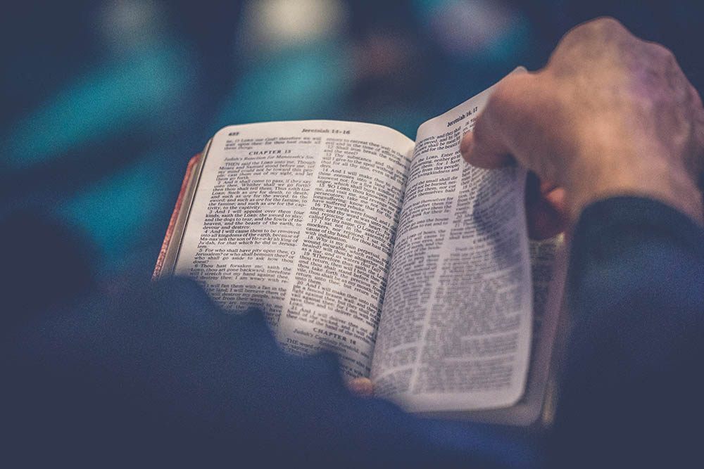 An open Bible shows Jeremiah chapter 13. A man's hand is turning the page.